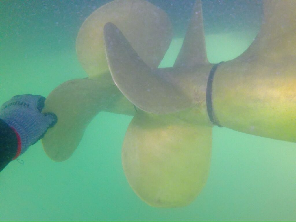 Barnacle King diver's gloved hand beside a cleaned bronze propeller underwater