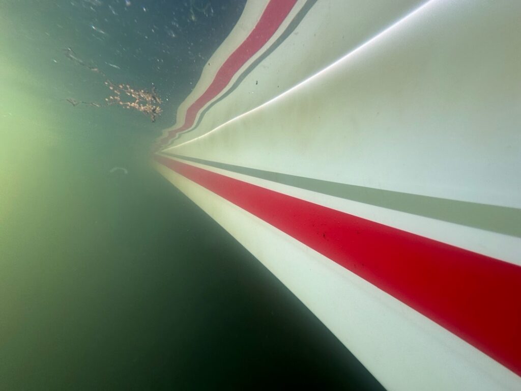Underwater view of a white boat hull with a red boot stripe below the waterline